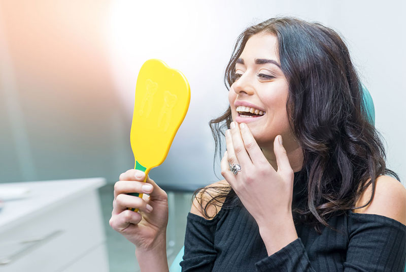 Lady smiling into mirror looking at her smile.